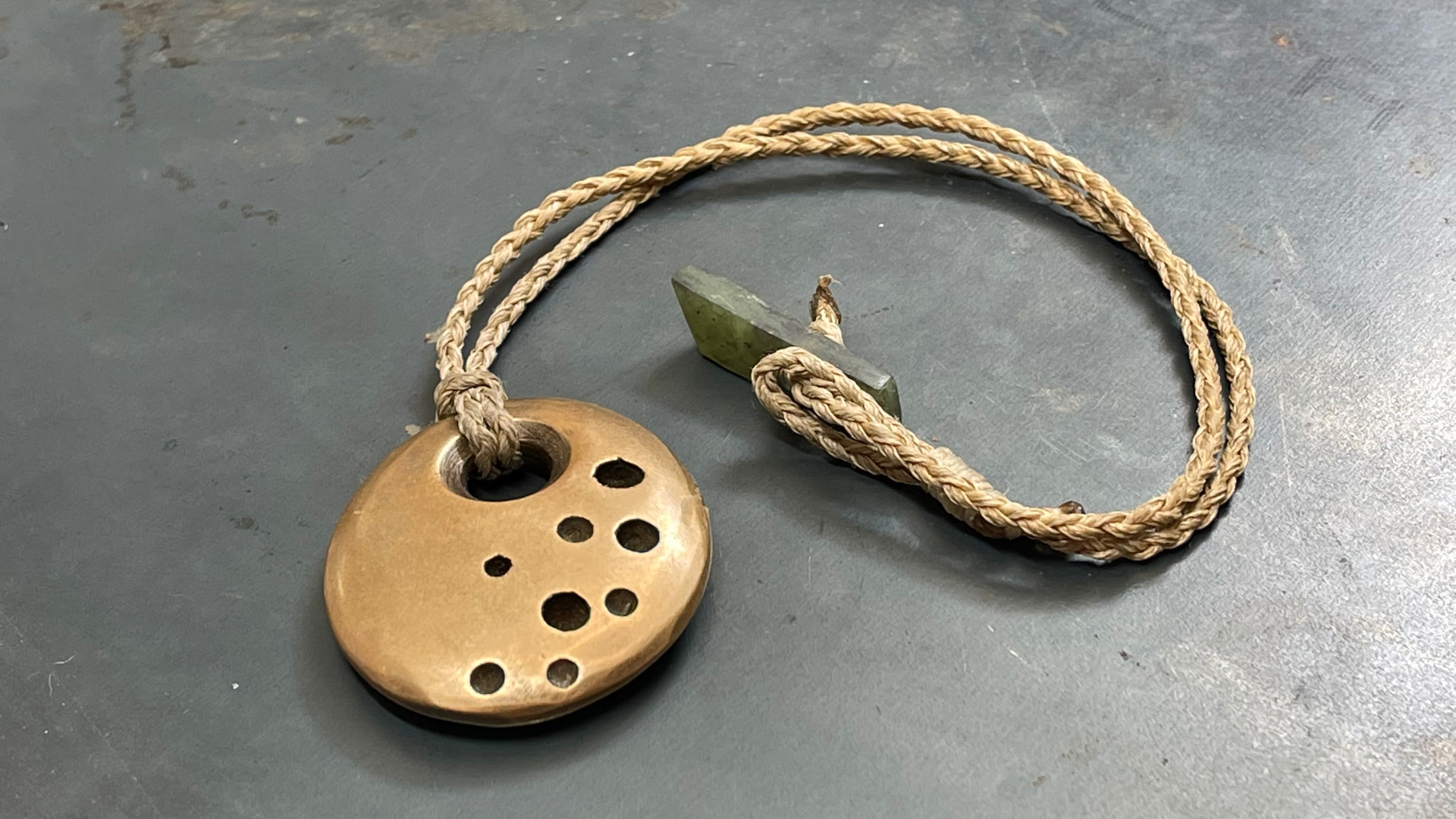 Pierced bronze pendant with pounamu toggle on braided cord